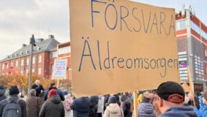 En person håller ett plakat med texten "Försvara äldreomsorgen"